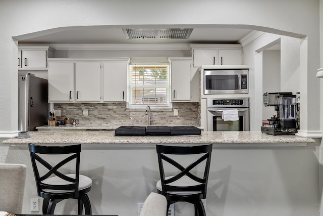 kitchen featuring a kitchen breakfast bar, light stone counters, stainless steel appliances, ornamental molding, and white cabinetry