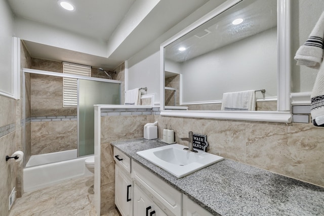 full bathroom with tile walls, combined bath / shower with glass door, vanity, and toilet