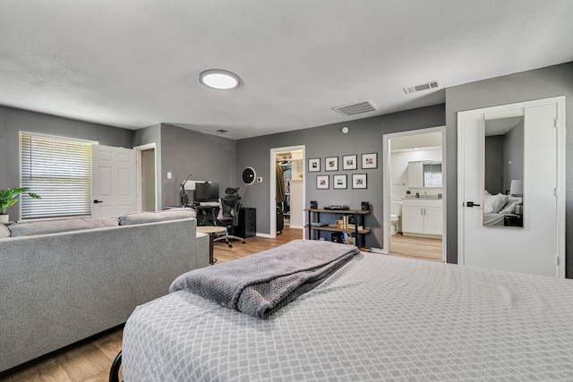 bedroom with light hardwood / wood-style floors, a walk in closet, and ensuite bath