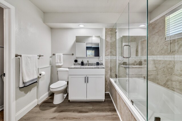 full bathroom featuring hardwood / wood-style floors, vanity, bath / shower combo with glass door, and toilet