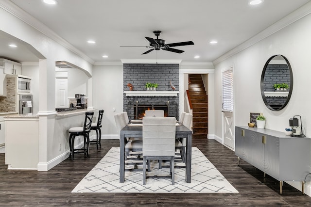 dining room featuring a brick fireplace, crown molding, ceiling fan, and dark wood-type flooring