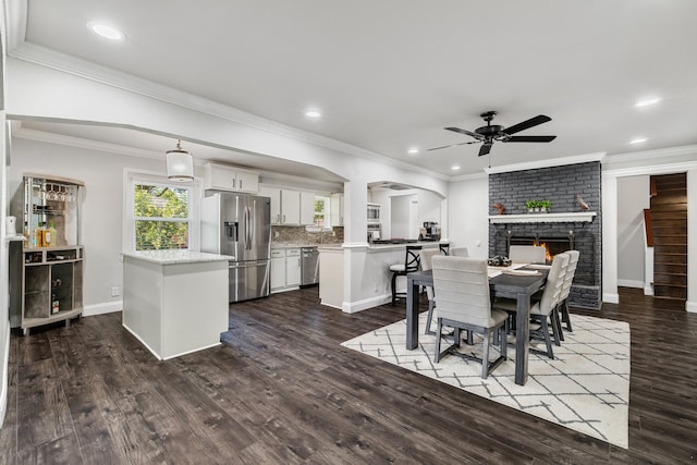 dining area featuring a brick fireplace, ceiling fan, and dark wood-type flooring