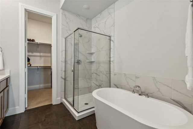 full bathroom with vanity, a freestanding tub, a marble finish shower, and a walk in closet