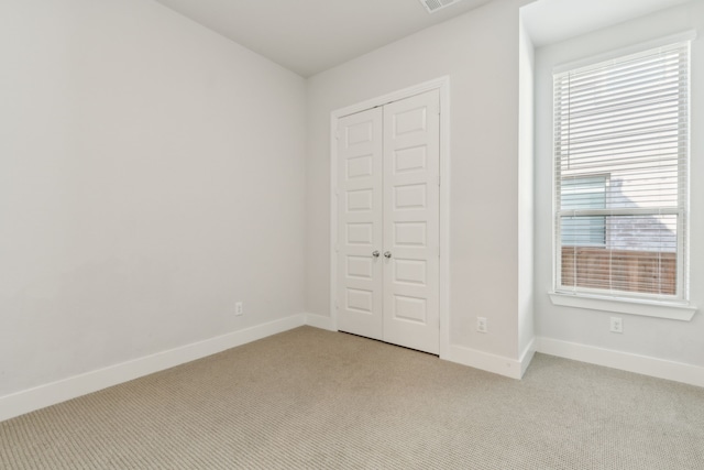 unfurnished bedroom featuring light carpet, visible vents, baseboards, and a closet