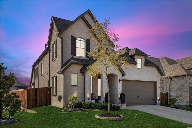 french country home featuring concrete driveway, an attached garage, fence, a yard, and brick siding