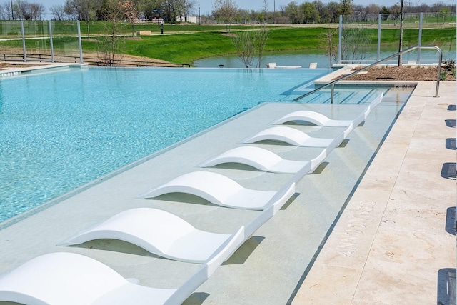 view of swimming pool with an infinity pool, a water view, and fence