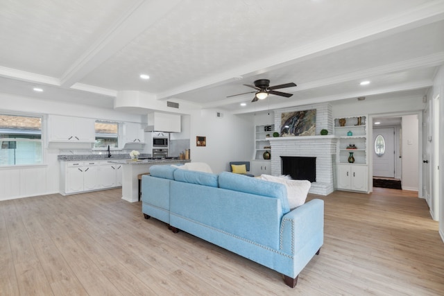 living room featuring a brick fireplace, light hardwood / wood-style floors, beam ceiling, and ceiling fan