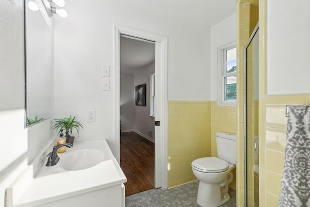 bathroom with toilet, wood-type flooring, tile walls, a shower with shower door, and vanity