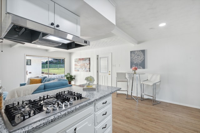 kitchen with light hardwood / wood-style flooring, range hood, stainless steel gas stovetop, light stone countertops, and white cabinetry