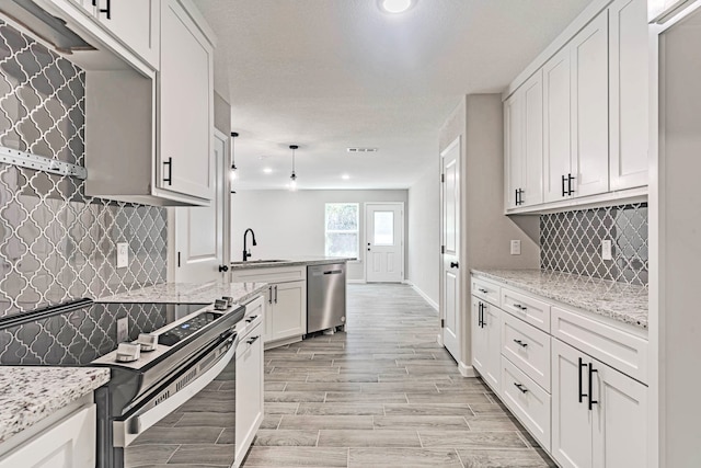 kitchen with light wood-type flooring, light stone countertops, decorative backsplash, white cabinets, and appliances with stainless steel finishes