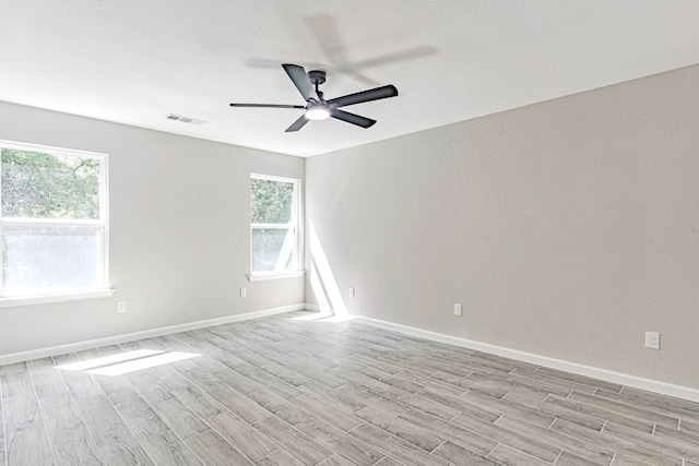 spare room with ceiling fan, light wood-type flooring, and a healthy amount of sunlight