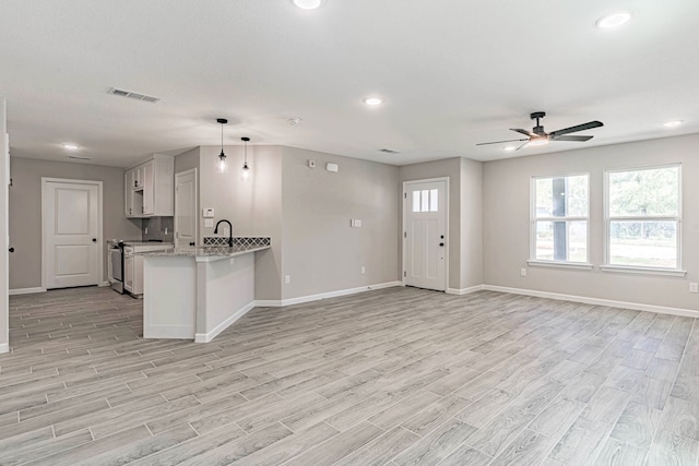 kitchen with pendant lighting, light hardwood / wood-style flooring, light stone countertops, kitchen peninsula, and white cabinetry