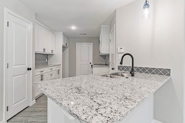 kitchen with kitchen peninsula, light stone counters, sink, and white cabinets