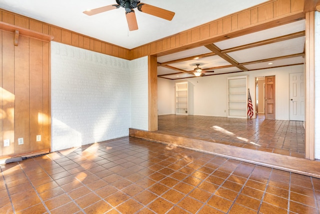 empty room with wood walls, beamed ceiling, coffered ceiling, and ceiling fan