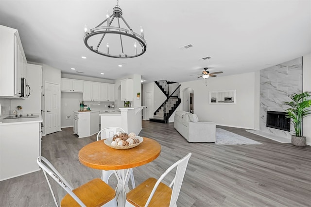 dining area featuring a fireplace, light hardwood / wood-style floors, and ceiling fan with notable chandelier