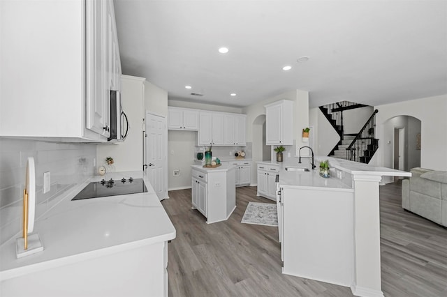 kitchen with a center island, kitchen peninsula, sink, white cabinetry, and light wood-type flooring