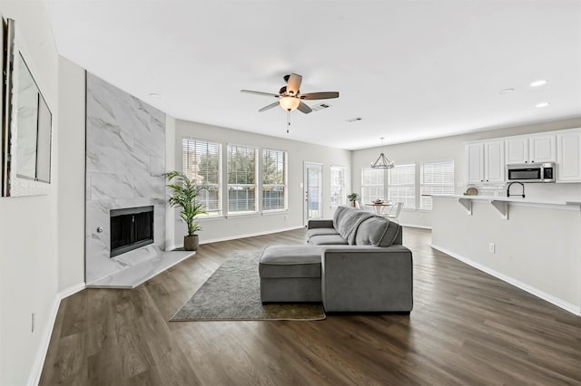 living room featuring a premium fireplace, plenty of natural light, dark hardwood / wood-style floors, and ceiling fan