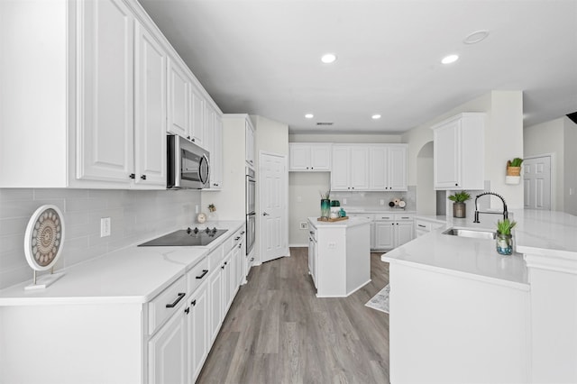 kitchen with light hardwood / wood-style floors, sink, kitchen peninsula, appliances with stainless steel finishes, and white cabinets