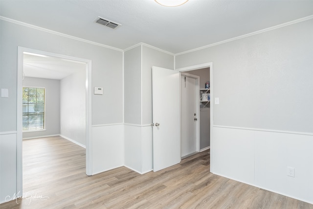 empty room with ornamental molding, light hardwood / wood-style flooring, and a textured ceiling