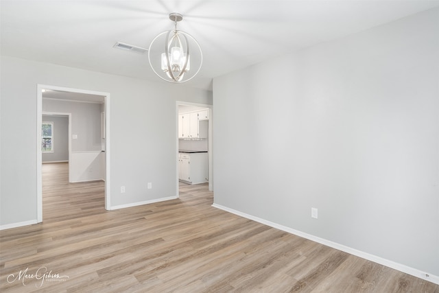 empty room with an inviting chandelier and light hardwood / wood-style flooring