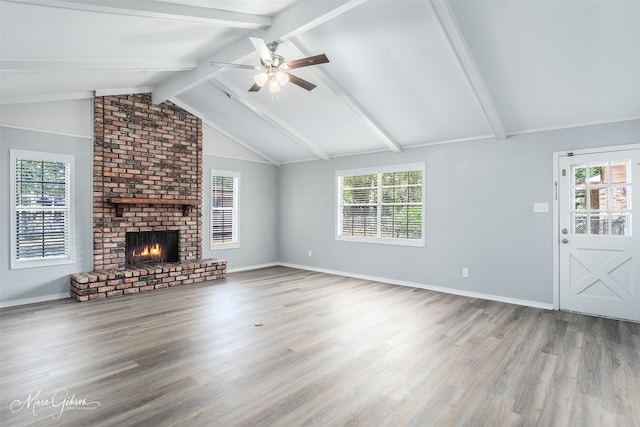 unfurnished living room with ceiling fan, a brick fireplace, vaulted ceiling with beams, and wood-type flooring