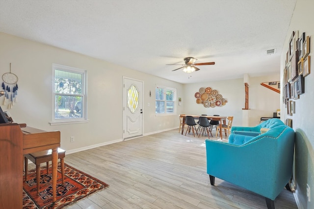 living room with a textured ceiling, light wood-type flooring, and ceiling fan