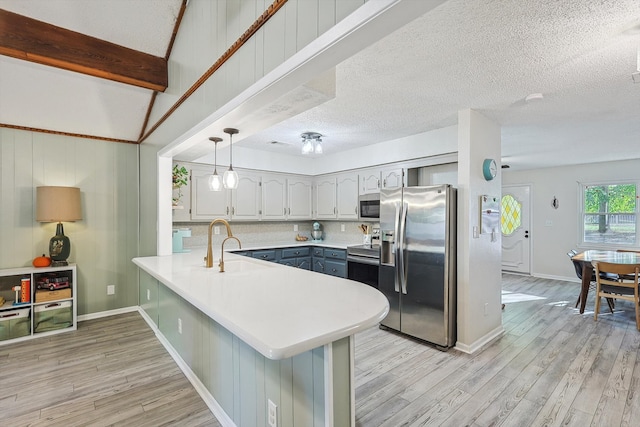 kitchen featuring a breakfast bar, appliances with stainless steel finishes, decorative light fixtures, light hardwood / wood-style floors, and kitchen peninsula