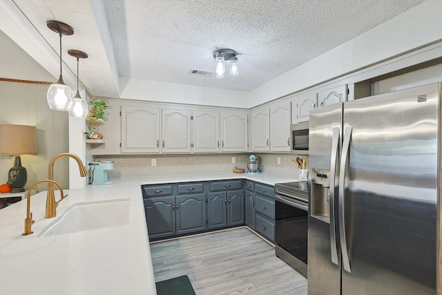 kitchen featuring sink, light hardwood / wood-style floors, a textured ceiling, decorative light fixtures, and appliances with stainless steel finishes