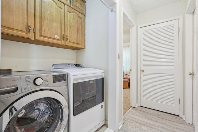 laundry area with cabinets, separate washer and dryer, a textured ceiling, and light hardwood / wood-style flooring