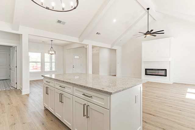 kitchen featuring lofted ceiling with beams, light wood-type flooring, light stone countertops, a center island, and pendant lighting