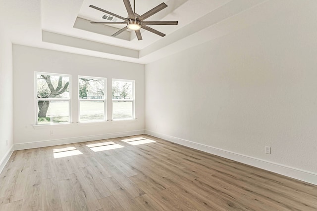 empty room featuring ceiling fan, a raised ceiling, and light hardwood / wood-style flooring