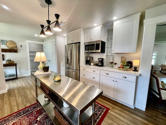 kitchen with hanging light fixtures, appliances with stainless steel finishes, hardwood / wood-style flooring, and white cabinetry