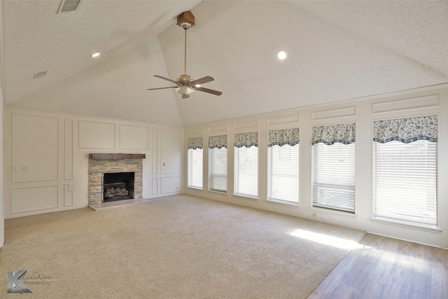 unfurnished living room with a wealth of natural light, ceiling fan, a stone fireplace, and light colored carpet