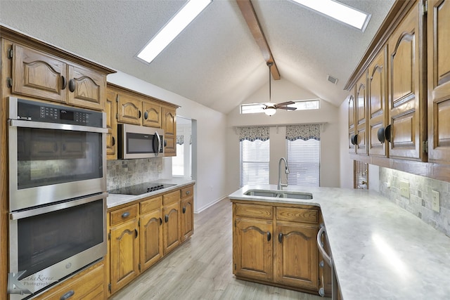 kitchen with lofted ceiling with beams, light wood-type flooring, appliances with stainless steel finishes, sink, and ceiling fan