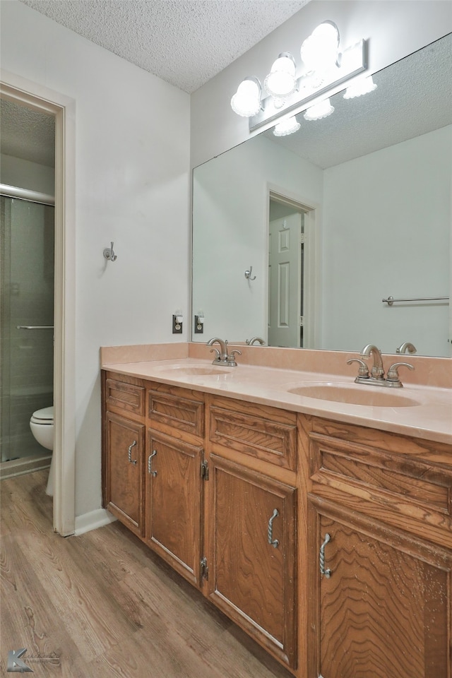 bathroom with hardwood / wood-style flooring, a textured ceiling, vanity, a shower with shower door, and toilet