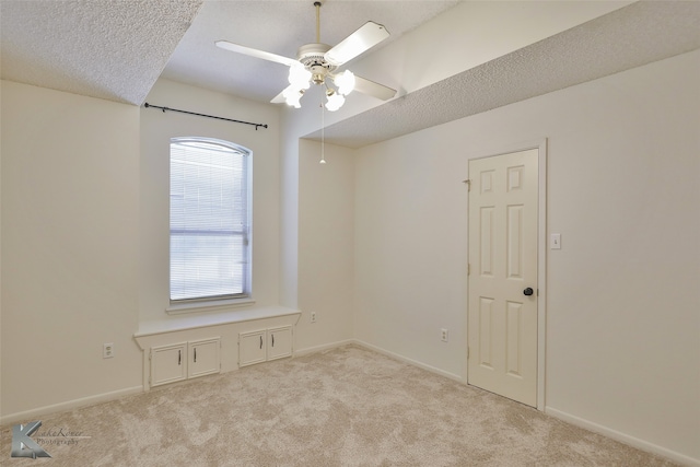 spare room with a textured ceiling, light colored carpet, and ceiling fan