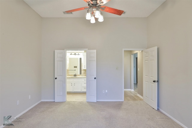 unfurnished bedroom featuring a towering ceiling, light carpet, sink, connected bathroom, and ceiling fan