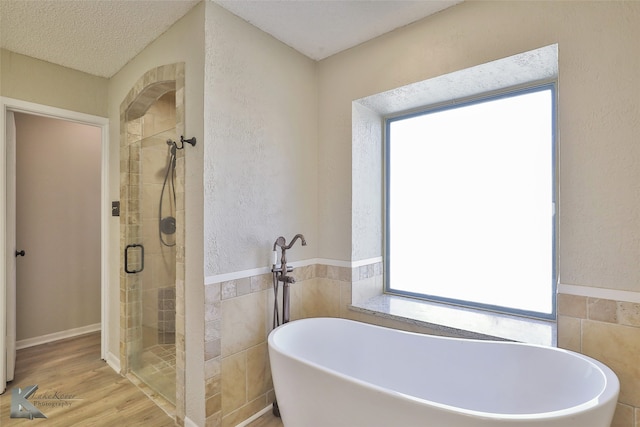 bathroom featuring wood-type flooring, a textured ceiling, shower with separate bathtub, and tile walls