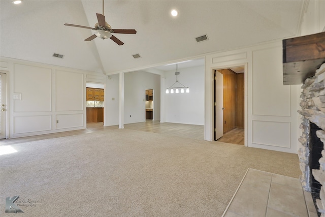 unfurnished living room featuring a stone fireplace, high vaulted ceiling, light carpet, and ceiling fan