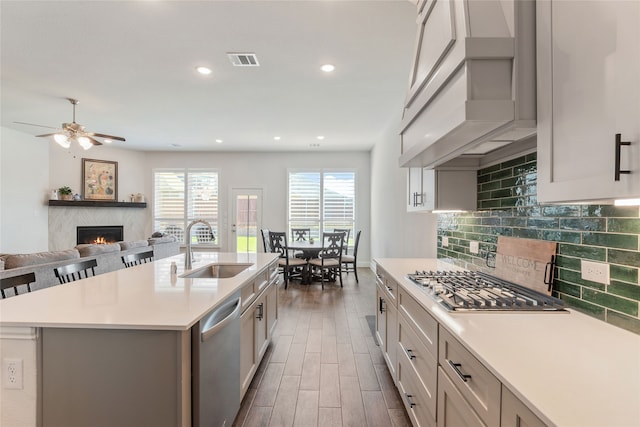 kitchen with an island with sink, stainless steel appliances, custom range hood, sink, and dark hardwood / wood-style flooring