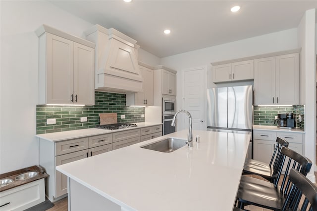 kitchen with a kitchen island with sink, dark wood-type flooring, sink, custom exhaust hood, and appliances with stainless steel finishes