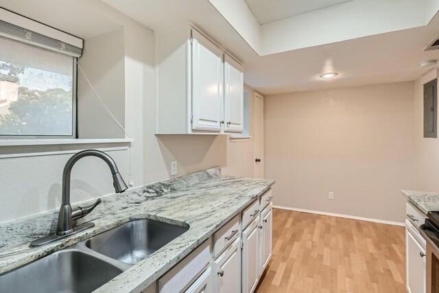 kitchen with light stone counters, electric panel, light hardwood / wood-style flooring, white cabinetry, and stainless steel appliances