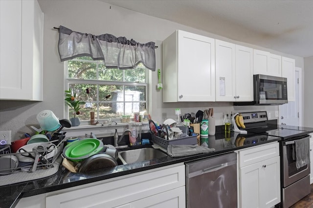 kitchen featuring appliances with stainless steel finishes, dark stone counters, and white cabinets