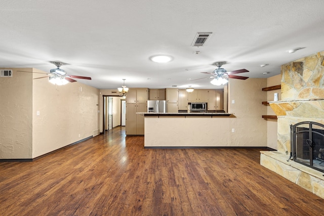 kitchen with a stone fireplace, a textured ceiling, appliances with stainless steel finishes, an inviting chandelier, and dark hardwood / wood-style flooring