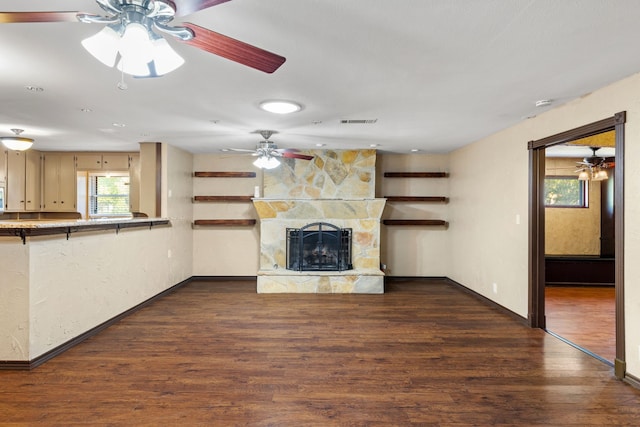 unfurnished living room featuring ceiling fan, a stone fireplace, and dark hardwood / wood-style floors