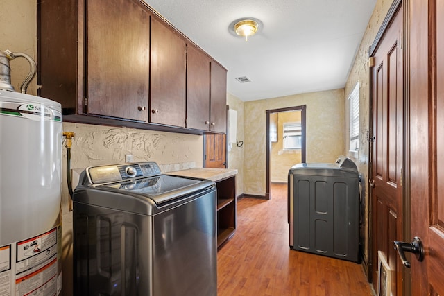 laundry area with light hardwood / wood-style floors, water heater, washer / clothes dryer, and cabinets