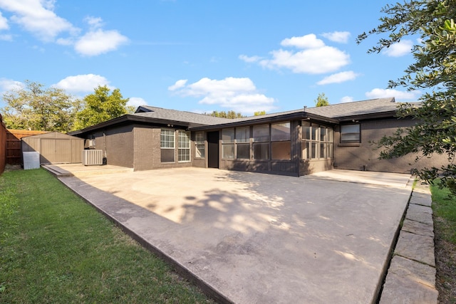 rear view of property featuring a patio, a storage shed, a sunroom, and a lawn