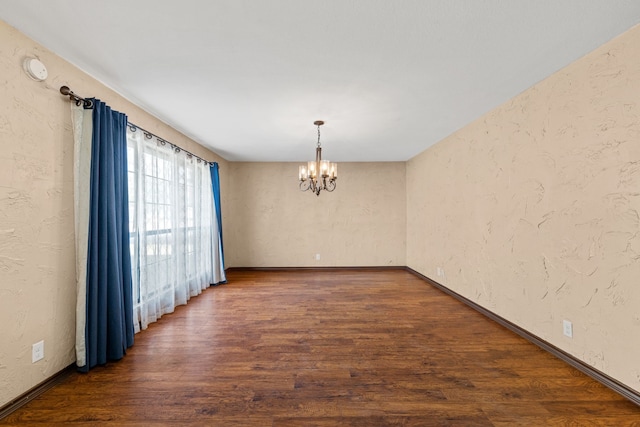 unfurnished room featuring an inviting chandelier and dark hardwood / wood-style flooring