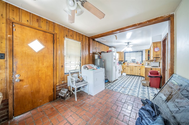 washroom featuring gas water heater, washer / dryer, ceiling fan, and wood walls