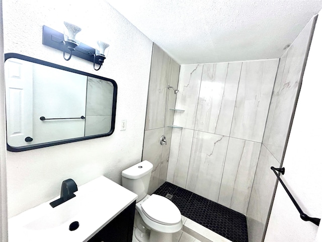 bathroom with toilet, vanity, a textured ceiling, and tiled shower